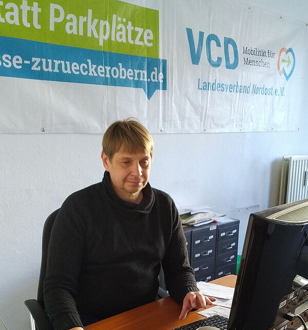 ein Mann am Schreibtisch, im Hintergrund ein VCD Banner