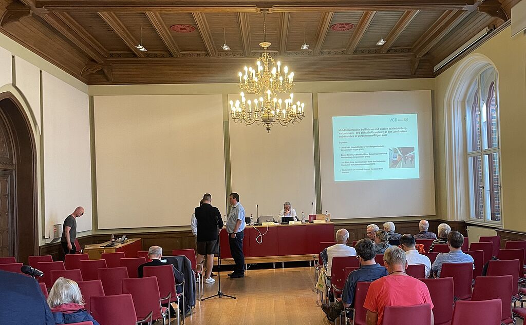 Mehere Menschen in einem Kirchartigen Raum mit Kronleuchter