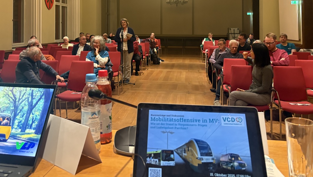 Ein Saal mit Menschen gefüllt, im Vordergrund ein Bildschirm